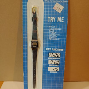 May include: A vintage Medana quartz watch on its original blue and white packaging. The watch has a black strap and a gold-coloured buckle and case. The packaging includes the text "TRY ME" and "FIVE FUNCTIONS".