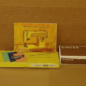 May include: A collection of vintage sewing accessories, including a Singer sewing machine instruction manual, a box of Singer needles, and a box of Wiss pinking shears. The instruction manual features a yellow sewing machine illustration.