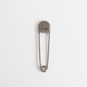 May include: A silver safety pin with a rounded head.