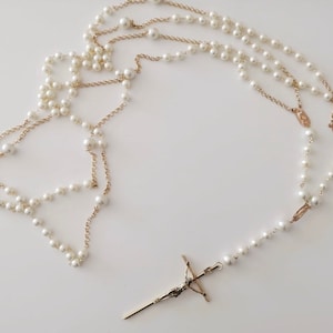 May include: A white pearl necklace with a gold chain and a gold cross pendant.
