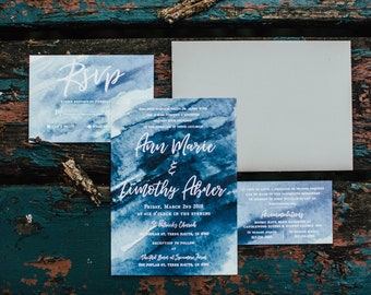 May include: Blue watercolor wedding invitation with white text. The invitation reads "Ann Marie & Timothy Abner" with the date and time of the wedding. The invitation also includes the location of the ceremony and reception.
