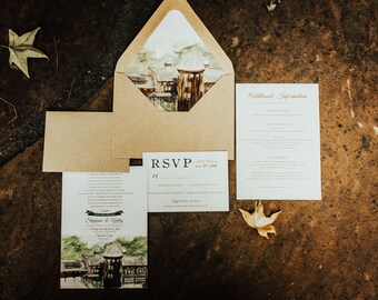 Puede incluir: Un conjunto de invitaciones de boda con una ilustración de acuarela de un edificio. La invitación está sobre un fondo marrón con un sobre marrón y una tarjeta RSVP blanca. El texto de la invitación dice "Stephanie & Colby".