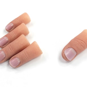 May include: Five realistic-looking silicone fingertip props, four are arranged in a pyramid shape, and one is laying flat. The fingertip props are skin-toned with pink fingernails.