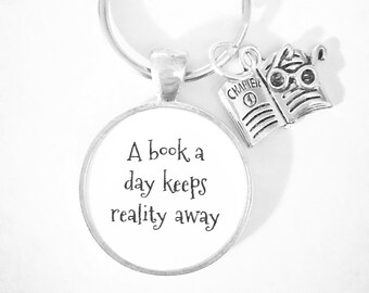May include: A silver keychain with a round charm that says "A book a day keeps reality away". The charm is attached to a silver key ring with a small silver book charm with glasses on top.