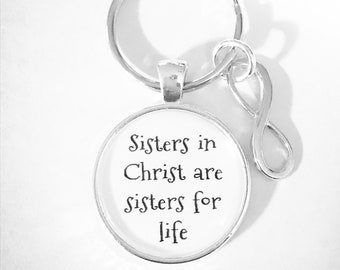 May include: Silver keychain with a round charm that says "Sisters in Christ are sisters for life". The charm is attached to a silver key ring with an infinity symbol.