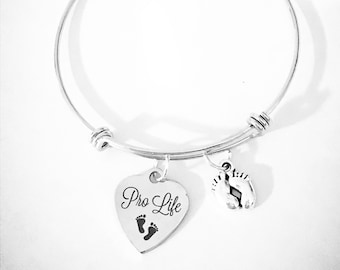 May include: Silver-toned bangle bracelet with two charms. One charm is a heart shape with the words "Pro Life" and two baby footprints. The other charm is a pair of baby feet.