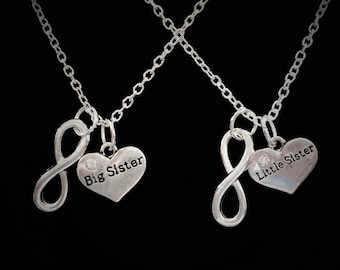 May include: Two silver necklaces with infinity symbols and heart pendants. The heart pendants say "Big Sister" and "Little Sister".