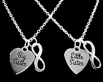 May include: Two silver necklaces with heart pendants. One pendant reads "Big Sister" and the other reads "Little Sister". Each necklace has an infinity symbol charm. The background is black.