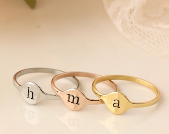 May include: Three gold, silver, and rose gold rings with initial engravings. The rings are stacked on top of each other. The initials are "h", "m", and "a".