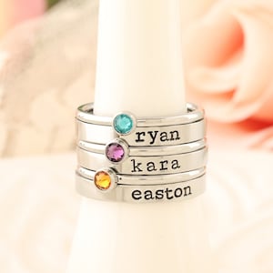 May include: Stackable rings with gemstones and engraved names "ryan", "kara", and "easton".
