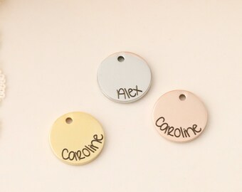 May include: Three round metal tags with names engraved on them. The tags are silver, gold, and rose gold. The names on the tags are Alex, Caroline, and Caroline.