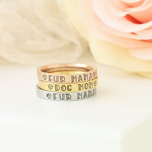 Puede incluir: Tres anillos apilados uno encima del otro en oro, plata y oro rosa. Los anillos est&aacute;n grabados con las palabras "Fur Mama" y "Dog Mom" con s&iacute;mbolos de huella de pata y coraz&oacute;n.