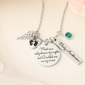May include: Silver necklace with a heart charm featuring a footprint design, a small angel wing charm, a round charm with the text "Most can only dream of angels, but I've held one in my arms", a green gemstone charm, and a rectangular charm with the text "Baby Anderson".