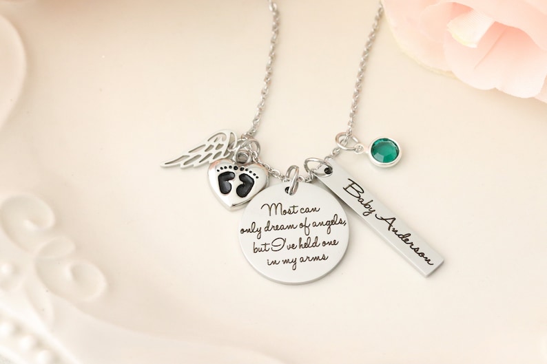 May include: Silver necklace with a heart charm featuring a footprint design, a small angel wing charm, a round charm with the text "Most can only dream of angels, but I've held one in my arms", a green gemstone charm, and a rectangular charm with the text "Baby Anderson".