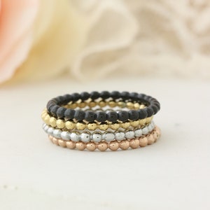 Puede incluir: Conjunto de cuatro anillos apilables con un dise&ntilde;o de cuentas. Los anillos son negros, dorados, plateados y de oro rosa.