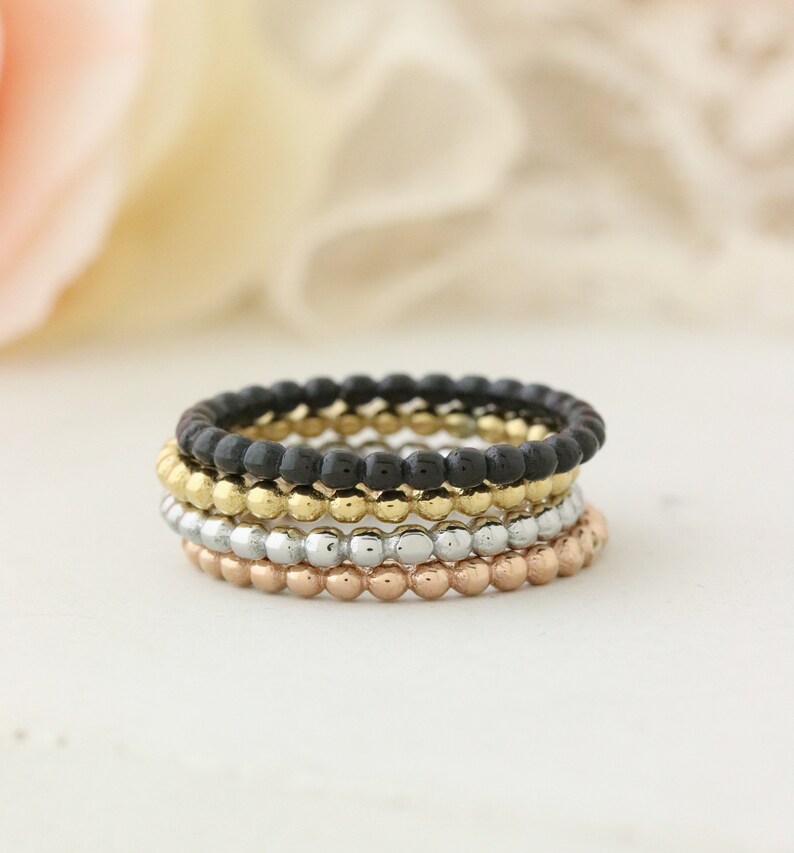 Puede incluir: Conjunto de cuatro anillos apilables con un dise&ntilde;o de cuentas. Los anillos son negros, dorados, plateados y de oro rosa.