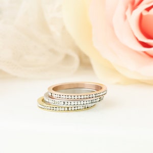 Puede incluir: Tres anillos finos de oro, plata y oro rosa con una fila de peque&ntilde;as piedras transparentes alrededor de cada banda.