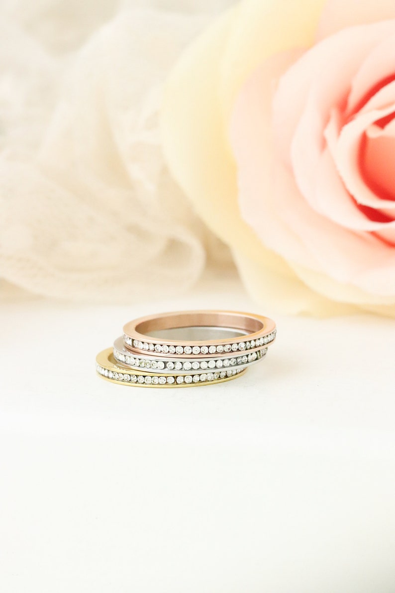 Puede incluir: Tres anillos finos de oro, plata y oro rosa con una fila de peque&ntilde;as piedras transparentes alrededor de cada banda.
