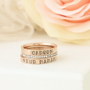 Puede incluir: Anillos apilables de oro rosa con las palabras "CARSON" y "FUR MAMA" grabadas. El anillo superior tiene una fila de piedras de circonita c&uacute;bica transparentes.