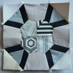 May include: A quilt block with a geometric design featuring black, white and grey fabric. The block is made up of 12 pieces of fabric, each with a different pattern. The centre of the block is a hexagon with a black and white striped pattern.