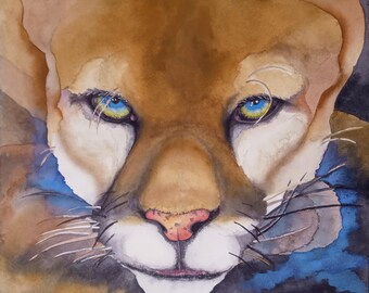 Puede incluir: Una pintura de acuarela de primer plano de la cara de un puma. El puma tiene ojos azules penetrantes y un pelaje marrón y blanco. El fondo es un azul y marrón borroso.