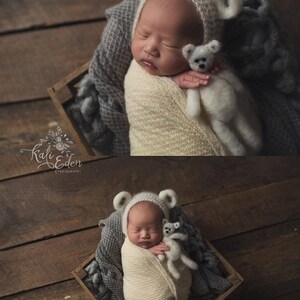 May include: A newborn baby wearing a white knitted bear hat and a white knitted blanket, sleeping in a wooden crate with a white knitted bear toy. The baby is surrounded by a gray knitted blanket.