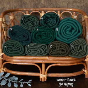 Puede incluir: Colección de nueve envolturas de tela verde enrolladas, exhibidas en una cesta de mimbre tejida. Las envolturas varían en tonos de verde, desde verde bosque profundo hasta oliva. La cesta es de mimbre marrón claro.