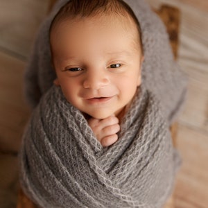 May include: A newborn baby wrapped in a gray knitted blanket, smiling up at the camera.