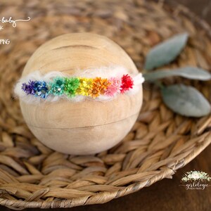 May include: A rainbow flower headband with white felt and colourful flowers. The headband is on a woven basket.