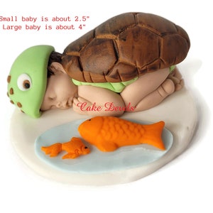 May include: A whimsical cake topper featuring a baby in a turtle shell, with a green turtle hat and a light green diaper. Two orange fish are on a light blue plate. The small baby is about 2.5 inches, and the large baby is about 4 inches.