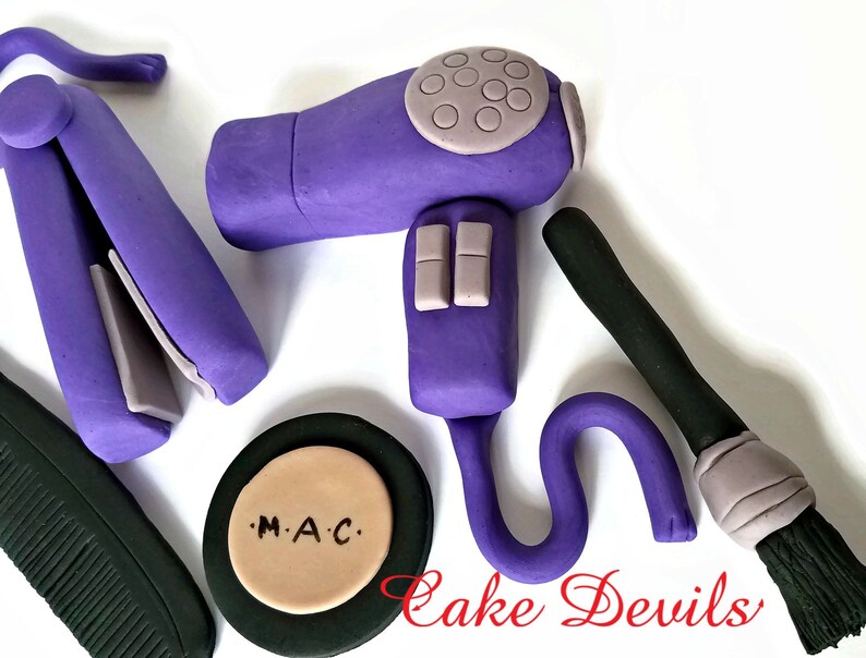 May include: Purple hair dryer, curling iron, makeup brush, and a compact with the text "M.A.C." on the lid. These are all fondant decorations for a cake.
