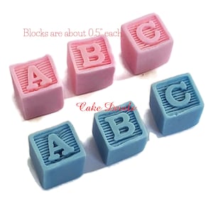 May include: Six pastel-colored alphabet blocks, each about 0.5 inches tall, spell out "ABC" in pink and blue. The blocks are made of fondant and are perfect for decorating cakes or cupcakes.