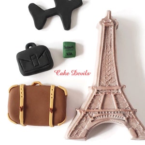 May include: A set of five fondant cake toppers featuring travel-themed items: a brown suitcase, a black briefcase, a black airplane, a green passport, and a brown Eiffel Tower.