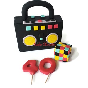 May include: A black and yellow boombox cake with a colorful Rubik's cube and red number candles that spell out "40".