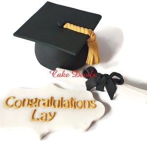 May include: A black graduation cap with a gold tassel, a white scroll tied with a black ribbon, and a white sign with gold lettering that says "Congratulations Lay".