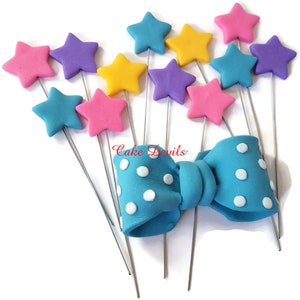 May include: A set of 10 cake toppers featuring a blue bow with white polka dots and 9 colorful stars on silver wires. The stars are pink, purple, yellow, and blue.