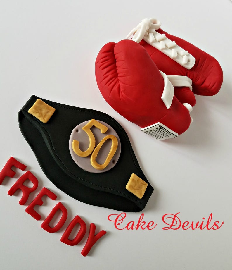 May include: Red boxing gloves with white laces, a black championship belt with a gold "50" on it, and the words "FREDDY Cake Devils" in red.