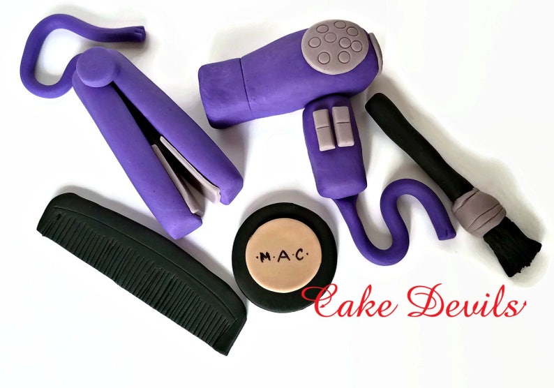 May include: Purple hair styling tools including a hairdryer, curling iron, comb, and makeup brush. A round compact with the text "M.A.C." is also included.