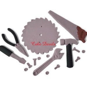 May include: A set of 10 fondant cake decorations shaped like tools, including a saw blade, a hammer, pliers, a wrench, a screwdriver, and nuts and bolts. The tools are all gray, black, and brown.