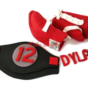 May include: Red boxing gloves with white laces and a black championship belt with a silver number 12 and the name Dylan in red letters.
