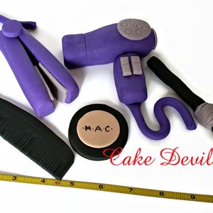 May include: Purple hair styling tools made of fondant, including a hairdryer, curling iron, comb, and a makeup compact with the text "M.A.C."