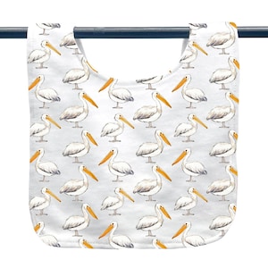 May include: A white baby bib with a repeating pattern of pelicans. Each pelican is depicted with white feathers, a gray back, and a long orange beak. The bib is made of soft fabric and has a curved shape.