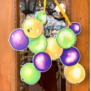 May include: A colorful, festive door decoration featuring a cluster of balloon-shaped cutouts in shades of yellow, green, and purple. The balloons are attached with a yellow ribbon. The word "SALON" is visible in the background.