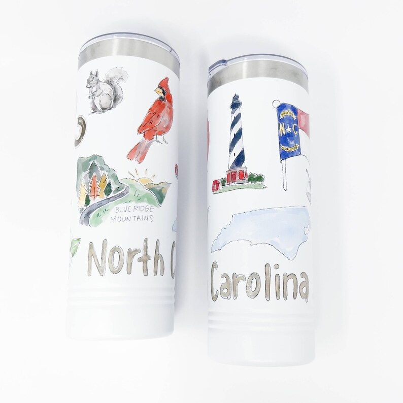 Pu&ograve; includere: Due bicchieri isolati bianchi con coperchi argentati. Uno presenta un'illustrazione di scoiattolo, cardinale e Blue Ridge Mountains con testo "North Carolina". L'altro ha un faro, la bandiera statale e il contorno dello stato con testo "Carolina".