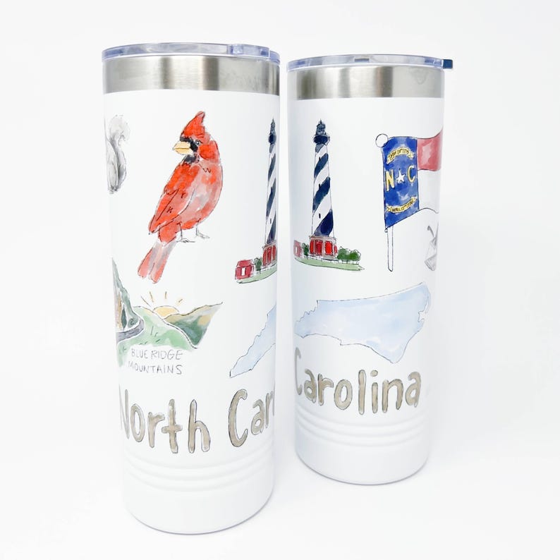 Pu&ograve; includere: Due bicchieri da viaggio bianchi in acciaio inossidabile con coperchi argentati. Ogni bicchiere presenta illustrazioni ad acquerello di monumenti della Carolina del Nord, tra cui un cardinale, un faro e la bandiera dello stato. Le parole "North Carolina" e "Carolina" sono stampate.