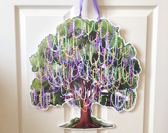 May include: A tree-shaped wall hanging with a green canopy and brown trunk, adorned with colorful beaded strands. The artwork is suspended by a purple ribbon, creating a festive and decorative piece. The design is reminiscent of Mardi Gras celebrations.