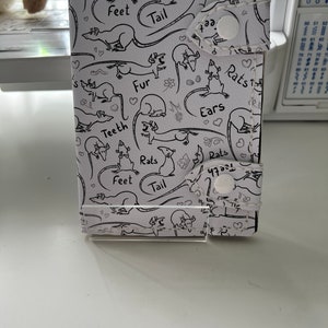 May include: A white fabric wallet with a repeating pattern of black and white rats. The pattern includes the words "Rats", "Feet", "Tail", "Fur", "Teeth", and "Ears".