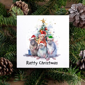 May include: A square Christmas card with a watercolour illustration of five rats wearing Santa hats in front of a Christmas tree. The card is surrounded by pine branches and pine cones. The text "Ratty Christmas" is printed at the bottom.