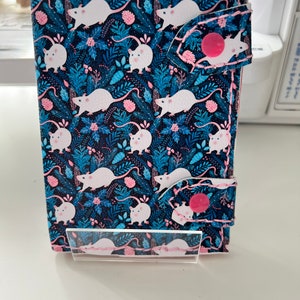 May include: A black leather wallet with a pink and blue floral pattern featuring white mice. The wallet has a pink snap closure.
