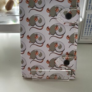 May include: A white leather wallet with a repeating pattern of sleeping mice. The wallet has two white flaps with black buttons.